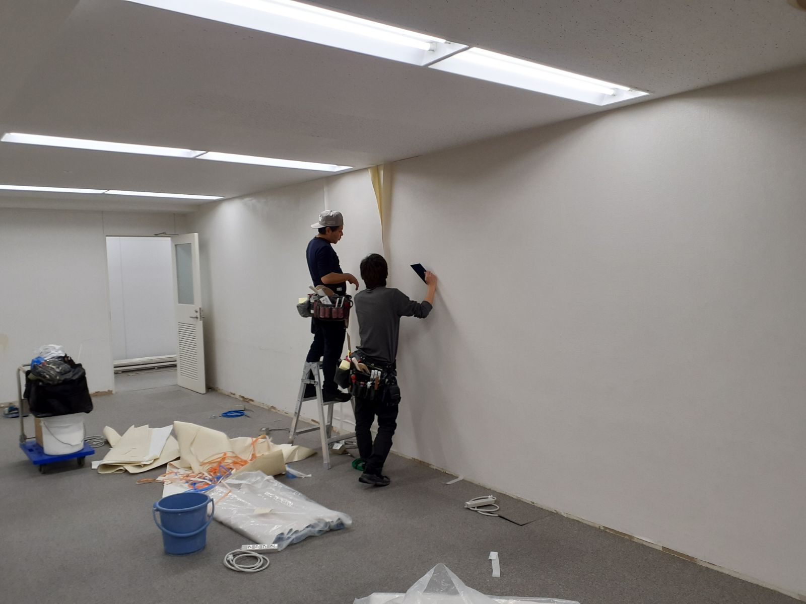 養生を施したオフィスで壁紙を丁寧に仕上げる2名の職人